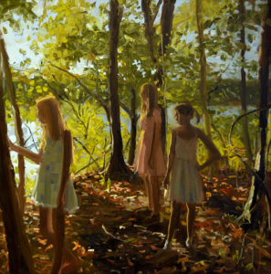 three girls stand on sunlit, wooded lakeshore